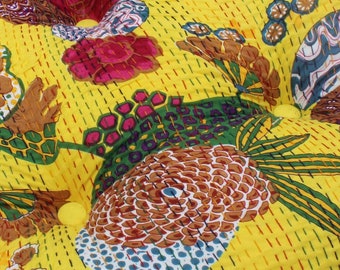 May include: A round yellow cushion with a floral pattern in shades of pink, brown, green, and blue. The cushion has a button in the center.