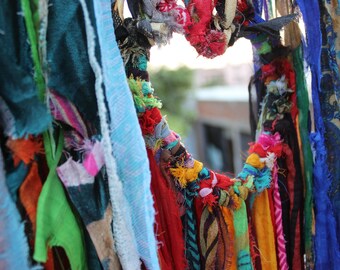 May include: A colorful display of fabric scraps tied together in a heart shape. The fabric is in various shades of blue, green, red, orange, yellow, and purple.