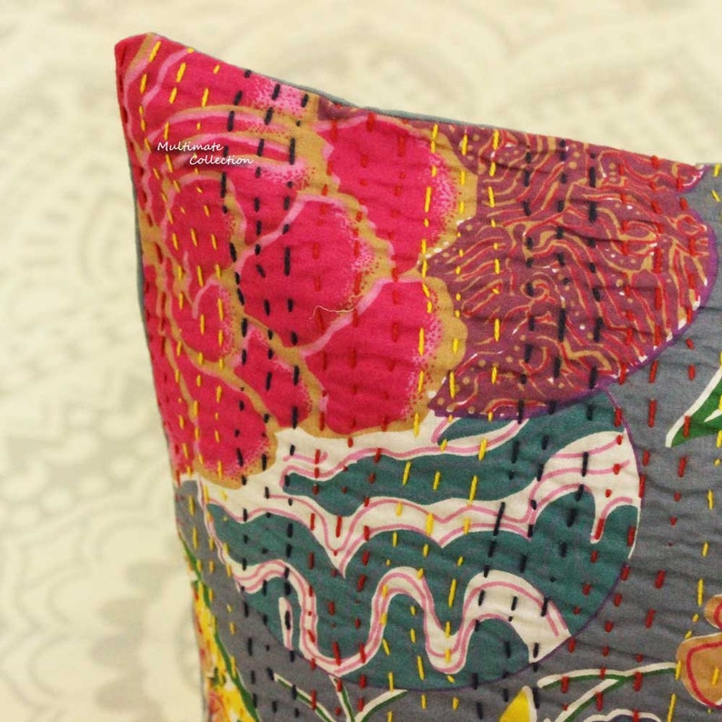 May include: A close-up of a gray and white pillow with a floral pattern. The pillow is made of kantha fabric and has a variety of colors, including pink, yellow, and green. The pillow is stitched with a variety of colors and patterns.