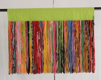 May include: A colorful curtain made of fabric strips hanging from a green fabric header. The strips are various colors, patterns, and textures.