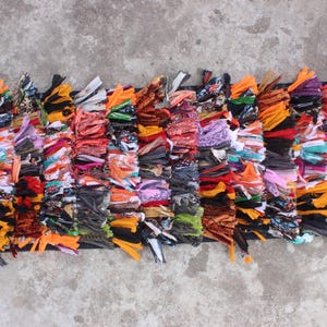 Può includere: Un tappeto colorato, multicolore, tessuto a mano con un bordo a frangia. Il tappeto è fatto di vari tessuti e trame, tra cui cotone, lana e seta. Il tappeto è lungo circa 90 cm e largo 30 cm.