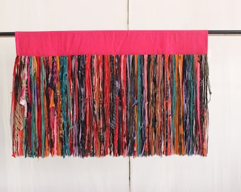 May include: A pink fabric valance with a long fringe of colorful fabric strips. The fringe is made of various colors, including red, orange, yellow, green, blue, purple, and brown.