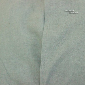 May include: A close-up of a light blue fabric with a single seam running down the center. The fabric has a subtle texture and a slightly faded appearance.