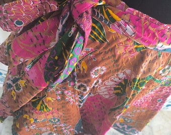 May include: A colorful wrap skirt with a floral pattern in shades of brown, pink, and green. The skirt is tied at the waist and features intricate stitching details. The fabric appears to be a patchwork design.