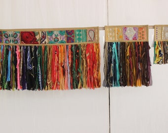 May include: Two colorful fabric wall hangings with fringe. The larger hanging has a patchwork design with a variety of colors and patterns. The smaller hanging has a similar design with a more muted color palette.