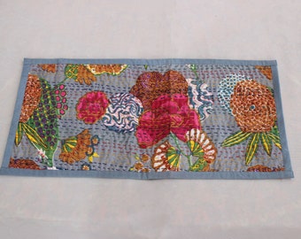 May include: A blue and white table runner with a floral pattern. The runner features a variety of flowers in shades of pink, orange, and green. The runner is quilted and has a blue border.