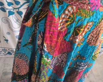 May include: A vibrant, patchwork wrap skirt in shades of turquoise, pink, and brown. The skirt features a tie closure and intricate stitching. The fabric is a mix of patterns and textures, creating a unique and colorful garment.