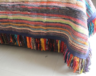 May include: A colorful, woven bedspread with a fringed edge. The bedspread features horizontal stripes in various colors, including red, orange, green, and blue. The fringed edge adds a decorative touch to the bedding.