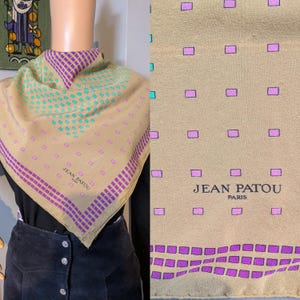 May include: A tan silk scarf with a geometric pattern and the text "JEAN PATOU PARIS". The scarf features purple and teal square designs and borders.