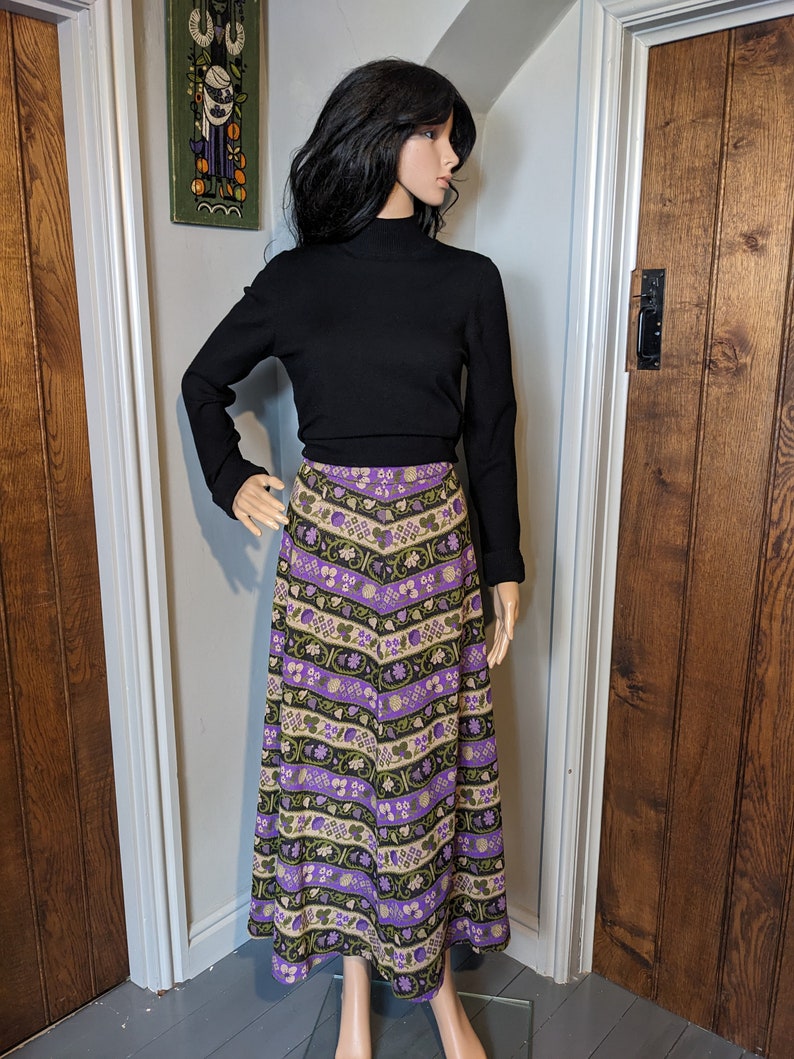 Puede incluir: Una falda larga y fluida con un estampado floral morado y verde. La falda est&aacute; hecha de una tela suave y tejida y tiene una cintura alta.