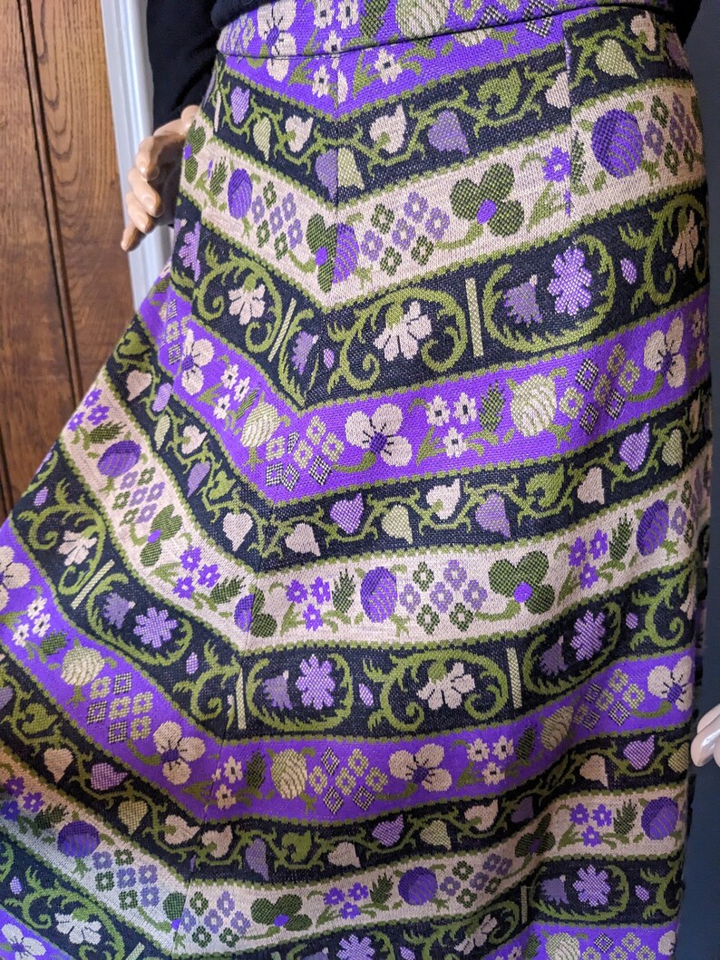 Puede incluir: Una falda morada, verde y negra con un estampado floral. La falda est&aacute; hecha de tejido tejido y tiene un estilo vintage.