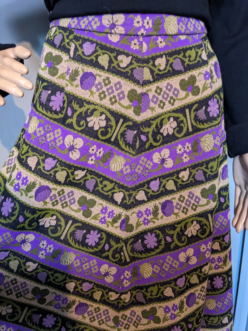 Puede incluir: Una falda de patr&oacute;n morado, verde y marr&oacute;n con un dise&ntilde;o floral. La falda est&aacute; hecha de tejido tejido y tiene una silueta ligeramente acampanada.