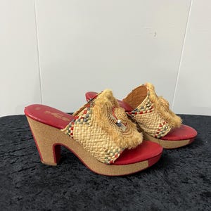 May include: Vintage red platform sandals with woven raffia detailing. The sandals have a cork wedge heel and a red leather footbed. The woven raffia is accented with colourful threads and a decorative embellishment.