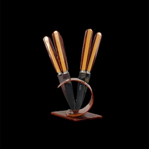 May include: Set of four knives with brown and yellow striped handles in a metal stand. The stand is shaped like a crescent moon.