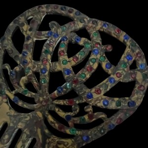 May include: An antique hair comb with a decorative openwork design. The comb is a mottled gold color and is embellished with red, green, and blue rhinestones. The comb's teeth are visible at the bottom of the image.