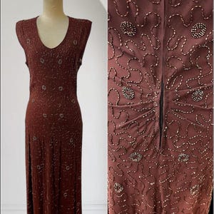 Puede incluir: Vestido marrón sin mangas con escote en V, exhibido en un maniquí. El vestido está adornado con intrincados abalorios y un patrón sutil. El vestido tiene una falda larga y cierre de cremallera en la espalda.