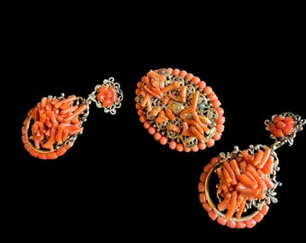 Puede incluir: Tres piezas de joyería de coral: un broche y dos pendientes. La joyería presenta piezas de coral de color naranja brillante engastadas en metal dorado. Los pendientes tienen forma de lágrima y el broche es ovalado.
