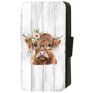 Pode incluir: Uma capa de telefone com um fundo de madeira branca e uma ilustração em aquarela de uma vaca Highland usando uma coroa de flores e óculos.
