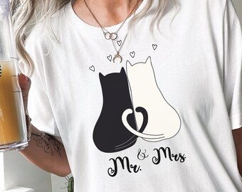 May include: White t-shirt with a black and white illustration of two cats with their tails intertwined. The text "Mr. & Mrs." is printed below the cats.