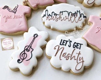 May include: Assortment of decorated sugar cookies with various Nashville-themed designs, including a guitar, a skyline, and the text "Let's Get Nashy".