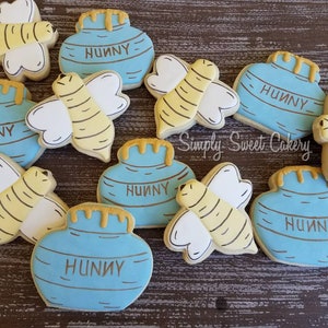 May include: A collection of nine decorated sugar cookies featuring a honey pot and bee theme. The cookies are decorated with blue and yellow icing and the words "Hunny" are written on the honey pot cookies.