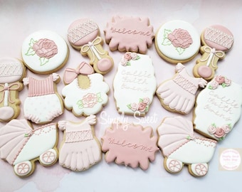 May include: A set of 15 pink and white decorated sugar cookies with various baby-themed designs, including a baby carriage, a rattle, a bib, and a dress. The cookies are decorated with pink and white icing and have the words "Callie Faith Bennett" and "Welcome" written on them.