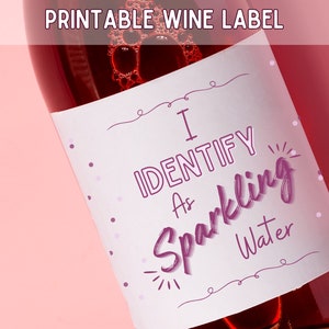 May include: A wine bottle with a label that reads "I Identify As Sparkling Water" in purple script. The label is white with purple polka dots and decorative lines. The top of the image says "Printable Wine Label".