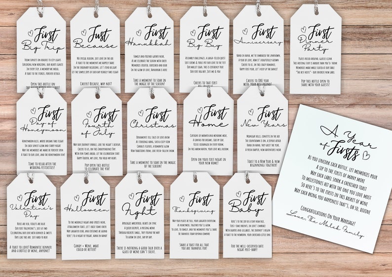 May include: A set of 14 white gift tags with black calligraphy. Each tag features a heart and the text "First" followed by a special occasion, such as "First Big Trip" or "First Christmas". The tags are arranged in two rows on a wooden surface. A white card with black calligraphy reads "A Year of Firsts" and includes a short message about celebrating milestones.