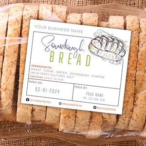 May include: A white label with green and blue text and a hand-drawn illustration of a loaf of sourdough bread. The label reads "Sourdough Bread" and lists the ingredients as "Wheat Flour, Water, Sourdough Starter (Wild Yeast Culture), Salt". It also states "Contains: Wheat, Gluten" and includes the date "03-01-2024" and the text "Made By: Your Name, Ph: 123-456-7881".