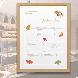 May include: A framed menu from Oak Street Bakery, featuring fall offerings. The menu is divided into sections for sourdough, fruit & nuts, savory, and sweet items. Decorative fall leaves accent the menu.