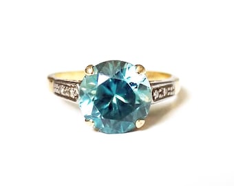 May include: A gold ring with a large, round, teal blue gemstone surrounded by smaller diamonds. The ring has a simple band.