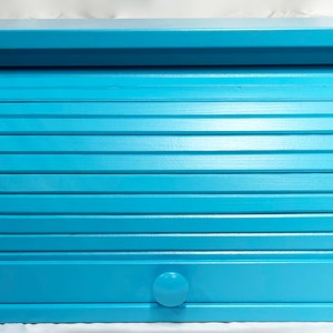 May include: A light blue wooden bread box with a roll-top lid and a small knob on the front.