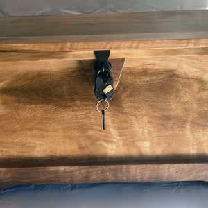 May include: A wooden storage chest with a dark brown stain and a black metal lock and key. The chest has a raised lip around the top and a base with a slight curve.