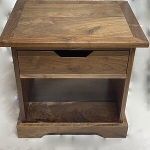 Puede incluir: Una mesa auxiliar de madera marr&oacute;n oscuro con un caj&oacute;n y un estante inferior. La mesa tiene un dise&ntilde;o simple y elegante y est&aacute; hecha de madera maciza.