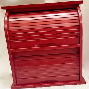 Puede incluir: Una caja de pan de madera roja con dos puertas enrollables. La caja de pan tiene una parte superior redondeada y una base rectangular.