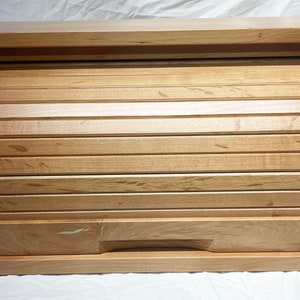 May include: A wooden bread box with a roll-top lid and a drawer. The box is made of light wood with a natural finish.