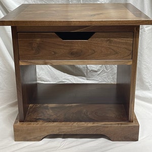 Puede incluir: Una mesa auxiliar de madera marr&oacute;n oscuro con un caj&oacute;n y un estante inferior. La mesa tiene un dise&ntilde;o simple y elegante y est&aacute; hecha de madera maciza.