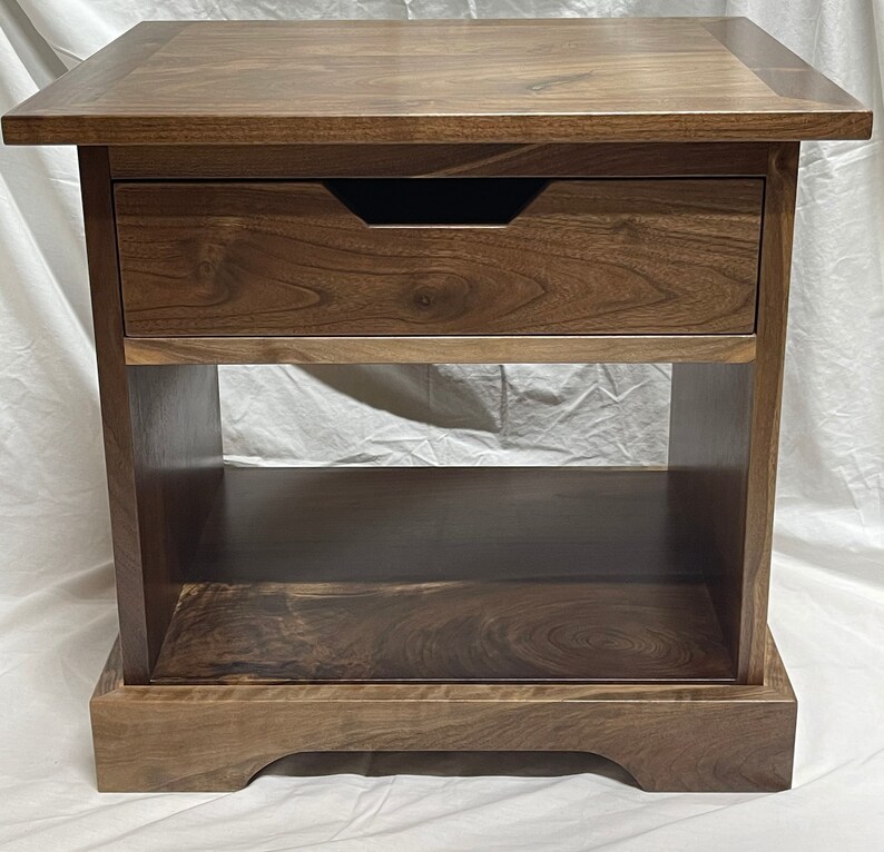 Puede incluir: Una mesa auxiliar de madera marr&oacute;n oscuro con un caj&oacute;n y un estante inferior. La mesa tiene un dise&ntilde;o simple y elegante y est&aacute; hecha de madera maciza.