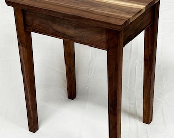 Puede incluir: Una mesa auxiliar de madera hecha a mano con una parte superior cuadrada y cuatro patas rectas. La mesa está hecha de madera marrón oscuro con un patrón de vetas natural. La mesa mide aproximadamente 61 cm de alto.