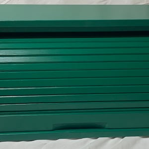 以下が含まれることがあります： ロールトップの蓋が付いた緑色の木製パン箱。蓋には、上下にスライドする水平なスラットが並んでいます。