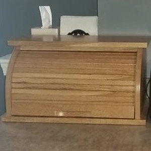 May include: A wooden bread box with a roll-top lid and a drawer. The box is made of light wood with a natural finish.