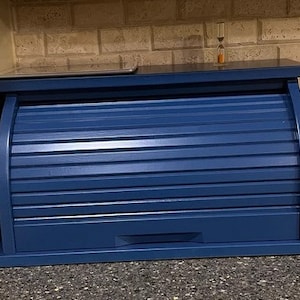 May include: A blue wooden bread box with a roll-top lid. The lid has horizontal slats and a small drawer at the bottom.