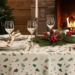 May include: A cream-coloured tablecloth featuring a repeating pattern of small green Christmas trees and tiny red stars. The table is set with white plates, clear wine glasses, a silver candle holder with a white taper candle, and a pine centrepiece.