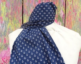 May include: A dark blue fabric scarf featuring a repeating white anchor pattern. The scarf is draped over a white mannequin form, displaying the nautical print clearly across the length of the material as it hangs down from the neck area.