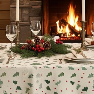 May include: A white tablecloth featuring a repeating pattern of small green Christmas trees and tiny red stars. The table is set with clear wine glasses, white plates, silver cutlery, and a centrepiece of pine branches, pinecones, and red berries.