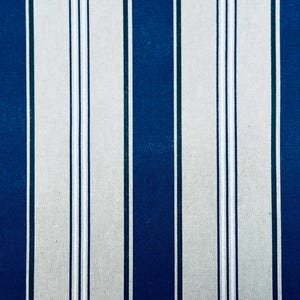 May include: A fabric pattern featuring vertical stripes in alternating widths. The design consists of wide navy blue bands separated by thinner white and light gray stripes, creating a repeating linear motif across the entire surface of the textile.