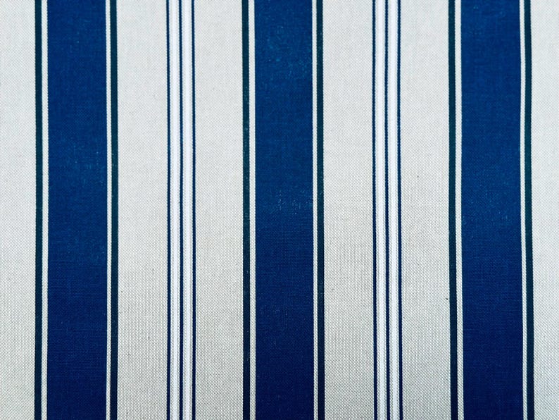 May include: A fabric pattern featuring vertical stripes in alternating widths. The design consists of wide navy blue bands separated by thinner white and light gray stripes, creating a repeating linear motif across the entire surface of the textile.