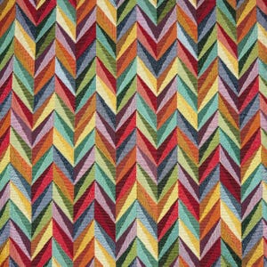 Op de afbeelding: Close-up van een veelkleurige stof met een chevronpatroon. Het zigzagpatroon herhaalt zich in tinten rood, oranje, geel, groen en blauw. De stof heeft een getextureerde uitstraling.