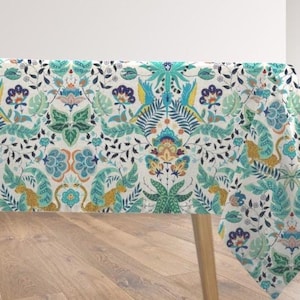 May include: A white tablecloth with a vibrant botanical pattern featuring teal, yellow, and green floral and animal motifs. The design includes stylized birds, flowers, and foliage, creating a decorative and colorful textile.