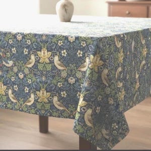 May include: A rectangular tablecloth featuring a dense, repeating pattern of birds, yellow flowers, and green foliage set against a deep blue background. The fabric drapes over the edges of a table, displaying a detailed botanical and avian design.